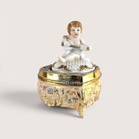 Vintage Hollywood Regency ornate gold metal footed trinket box featuring a small cherub figurine playing a lute on the lid.
