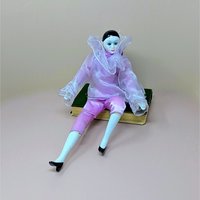 A 16-inch vintage Pierrot clown doll wearing a pink satin and sheer organza outfit, sitting on a green book against a neutral background.