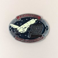A commemorative oval belt buckle from 1986 featuring the Space Shuttle Challenger and a scroll listing the seven fallen crew members.