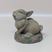 A hand-painted resin sculpture of a rabbit named Twitch scratching its ear on a mossy, leaf-strewn base against a neutral background.