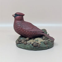 A hand-painted resin sculpture of a red cardinal perched on a bed of acorns and green leaves against a neutral background.
