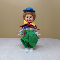 A vintage 10-inch Horsman clown doll with brown hair and a blue hat wearing a colorful mismatched outfit of stripes and polka dots against a neutral background.