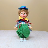 A vintage 10-inch Horsman clown doll with brown hair and a blue hat wearing a colorful mismatched outfit of stripes and polka dots against a neutral background.