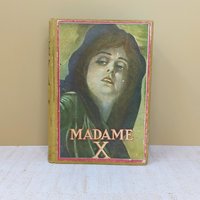 A tan cloth-bound antique book with a large, colorful lithograph pastedown on the front cover featuring a woman's portrait and the title Madame X against a neutral background.