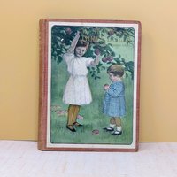 An antique children's book with a large color lithograph pastedown on the front cover depicting two young girls in an orchard against a neutral background.
