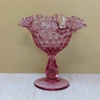A vibrant cranberry-colored glass candy dish with a thumbprint pattern and a ruffled rim on a pedestal base against a neutral background.