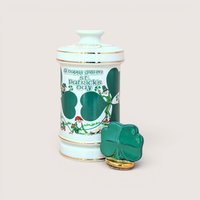 A tall white porcelain decanter featuring green "A Happy Green St. Patrick’s Day" typography, leprechaun illustrations, and a gold-trimmed shamrock stopper against a neutral background.