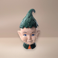 Large ceramic pixie elf cookie jar. Features a smiling face with blue eyes, pointed ears, and a vibrant green leaf-textured hat that serves as the lid. High-gloss glazed finish with deep green and warm flesh tones.