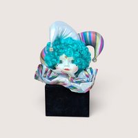 Porcelain jester doll head with bright teal curly hair and a striped hat, emerging from a black square base.