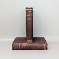 Two antique burgundy cloth-bound books stacked horizontally, showing gilded spine titles for The Life of Gladstone by John Morley.