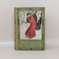 A vintage hardcover book titled Miss Nonentity by Mrs. L.T. Meade, featuring a pictorial cover of a woman in a red winter coat against a snowy background with green floral borders.