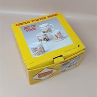 A yellow vintage box containing a set of four white ceramic mugs, each featuring a different colorful vintage circus poster illustration.