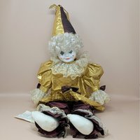 A large porcelain clown doll in a metallic gold and burgundy costume, wearing a tall pointed hat and featuring a white curly wig and hand-painted face.