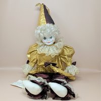 A large porcelain clown doll in a metallic gold and burgundy costume, wearing a tall pointed hat and featuring a white curly wig and hand-painted face.