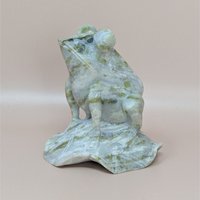 A vintage hand-carved nephrite jade figurine of a frog perched on a lily pad, showing natural pale green and olive marbling throughout the stone.