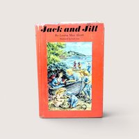 A vintage 1956 hardcover edition of Jack and Jill by Louisa May Alcott with a bright red dust jacket featuring children playing at the beach