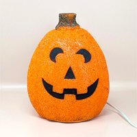 A vintage orange melted plastic "popcorn" Jack O'Lantern light with a smiling black face and a green stem on top.