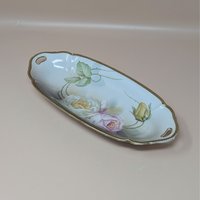 A vintage porcelain celery tray from Suhl, Germany, featuring a long oval shape with hand-painted yellow and pink roses and a worn gold rim.
