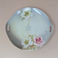 A vintage round porcelain dresser tray from PV Vessra Germany, featuring hand-painted white and pink lilies against a soft grey and cream background with gold trim.