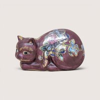 A mauve ceramic reclining cat figurine with gold and floral details, centered on a beige background.