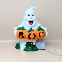 A hand painted vintage white ceramic ghost holding three orange pumpkins that spell out BOO with a small grey RIP tombstone at the base