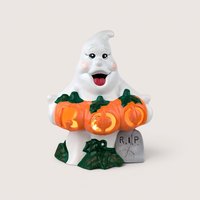 A lit ceramic ghost figurine holding orange pumpkins that spell "BOO," centered on a beige background.A lit ceramic ghost figurine holding orange pumpkins that spell "BOO," centered on a beige background.