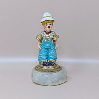 A vintage hand painted clown figurine by Ron Lee named Rascal, wearing blue overalls and a white hat, mounted on a thick natural onyx stone base