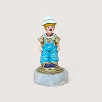 A small clown figurine in blue overalls and a white hat on a quartz base, centered on a beige background.