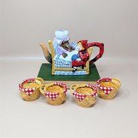 A colorful Dept 56 ceramic teapot set showing Little Red Riding Hood sitting by the Big Bad Wolf in a bed, accompanied by four small tea cups shaped like wicker picnic baskets