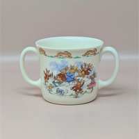 A vintage cream colored two handled mug featuring a group of rabbits on a sled with a border of running rabbits around the rim