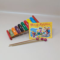 A vintage colorful metal xylophone with eight rainbow colored keys alongside three wooden mallets and a yellow music instruction sheet featuring cartoon animals