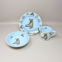 A three piece Royal Worcester porcelain nursery set including a plate, bowl, and mug featuring a teddy bear and the Monday's Child poem