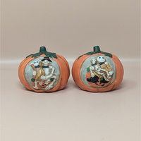 Two orange ceramic pumpkin candle holders featuring relief carvings of skeleton couples in formal wear within a light grey medallion