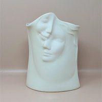 Front view of a white porcelain vase featuring two serene faces in relief. The faces overlap with soft, flowing lines against a neutral background.