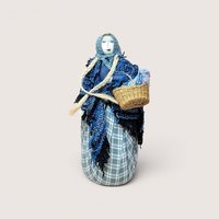 A handcrafted textile doll with long black hair holding a small basket, centered on a beige background.