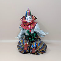 A vintage posable clown doll with a porcelain face and hands wearing a metallic silver and rainbow striped costume with a large ruffled collar.
