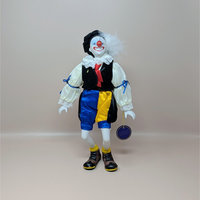 A vintage Royal Heirloom Collection clown doll with a white ceramic face, red nose, and a feathered black hat. It wears a velvet vest and multi-colored satin bloomers with blue ribbon accents.