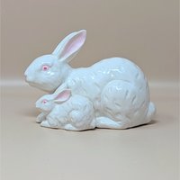 A vintage white ceramic figurine by Rosenthal Netter featuring a mother rabbit and her baby tucked beside her. The bunnies have pink eyes and ears with a subtle textured fur pattern in the glaze.