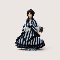 A vintage Peggy Nisbet costume doll in a black and white striped gown with ruffles, centered on a beige background.