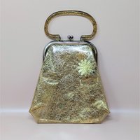 A 1960s clear vinyl handbag filled with shimmering gold tinsel and glitter. It features a trapezoid shape, a gold glitter-infused plastic handle, and a silver-tone metal clasp.