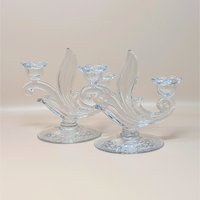 A pair of vintage clear glass double candlesticks by Duncan Miller in the First Love pattern. The holders feature elegant sweeping curves, flower-shaped candle cups, and an intricate etched floral design on the circular bases.