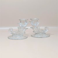 A pair of vintage clear glass cornucopia-shaped candlesticks by Fostoria in the Navarre pattern. The holders feature a decorative Baroque scroll design and an intricate etched floral pattern on the circular bases.