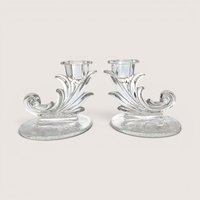 A pair of vintage clear glass cornucopia or leaf-shaped single candlestick holders, centered on a beige background.