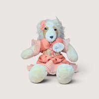 Plush teddy bear with white fur and brown eye patches wearing a peach dress, centered on a plain linen background.
