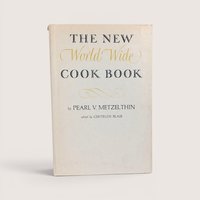 Vintage cookbook titled The New World Wide Cook Book by Pearl V Metzelthin centered on a plain linen background.