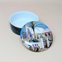 A vintage Goebel ceramic covered trinket box featuring the "Bermuda Gate" watercolor artwork by Eliot O'Hara. The round box has a dark textured exterior and a lid depicting a tropical scene with a palm tree, stone gate, and figures.