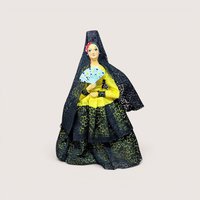 Vintage Spanish flamenco dancer doll wearing a yellow dress and black lace mantilla while holding a fan, centered on a plain linen background.