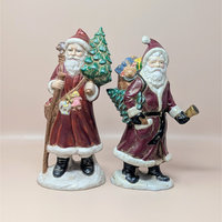 A vintage pair of large hand-painted ceramic Santa figures from the 1980s. Both wear deep red coats with faux fur trim, carry toy-filled sacks, and one holds a small Christmas tree while the other holds a bell.