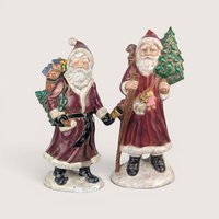 Pair of vintage Santa Claus figurines carrying Christmas trees and sacks of toys, centered on a plain linen background.
