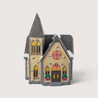 A 10-inch vintage 1988 Department 56 Snow Village Redeemer Church ceramic building with a tall steeple, stone-textured walls, lit windows, and festive wreaths.